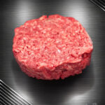 Rohes Haché Schweine-Burger Pattie aus grob gehacktem Schweinefleisch mit sichtbarer Struktur auf neutralem Untergrund.