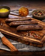 Zubereitete Wagyu Bratwurst aus Deutschland mit goldbrauner Kruste auf rustikalem Holzbrett angerichtet
